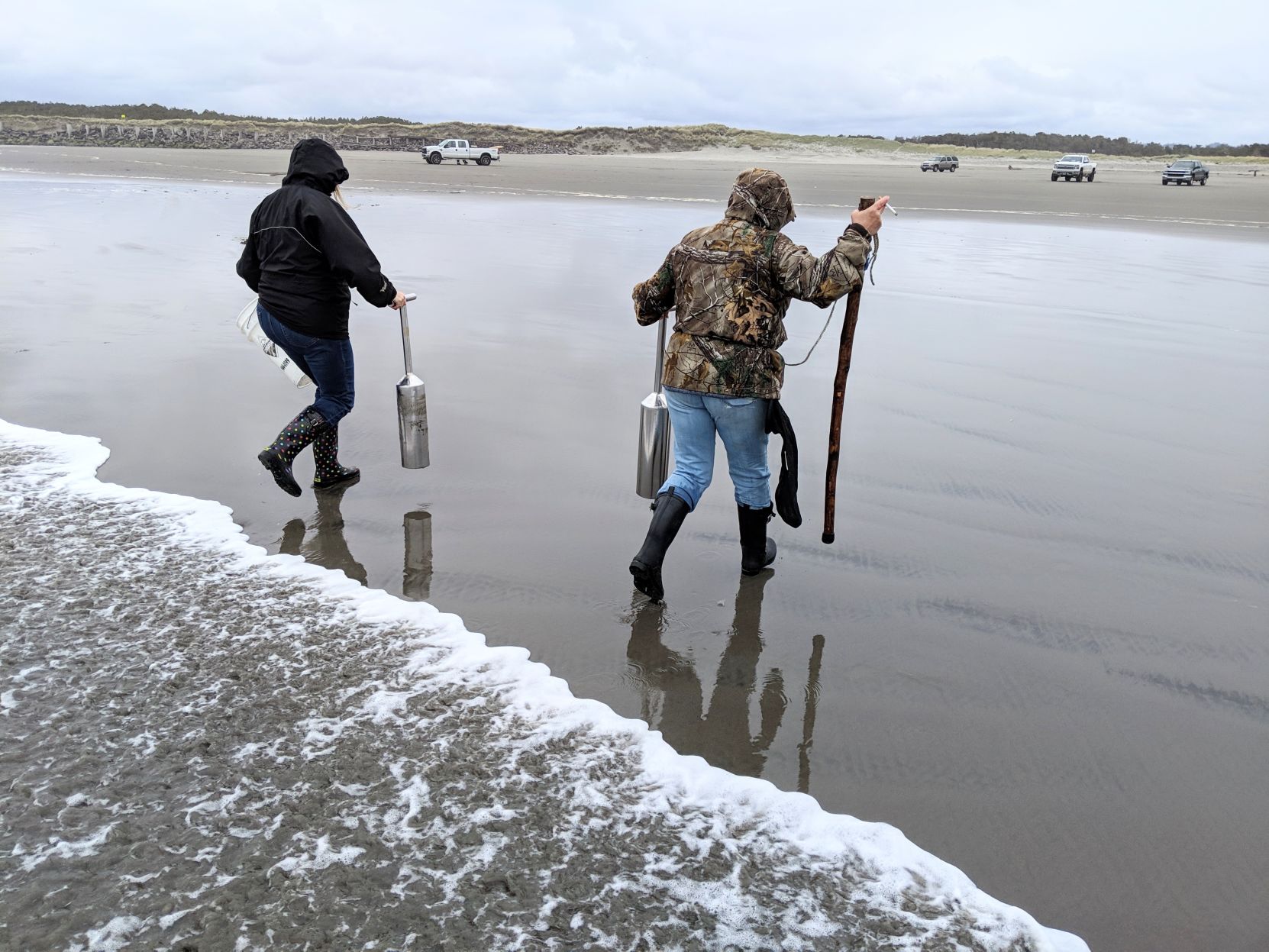 Women dodge waves while digging for razor clams